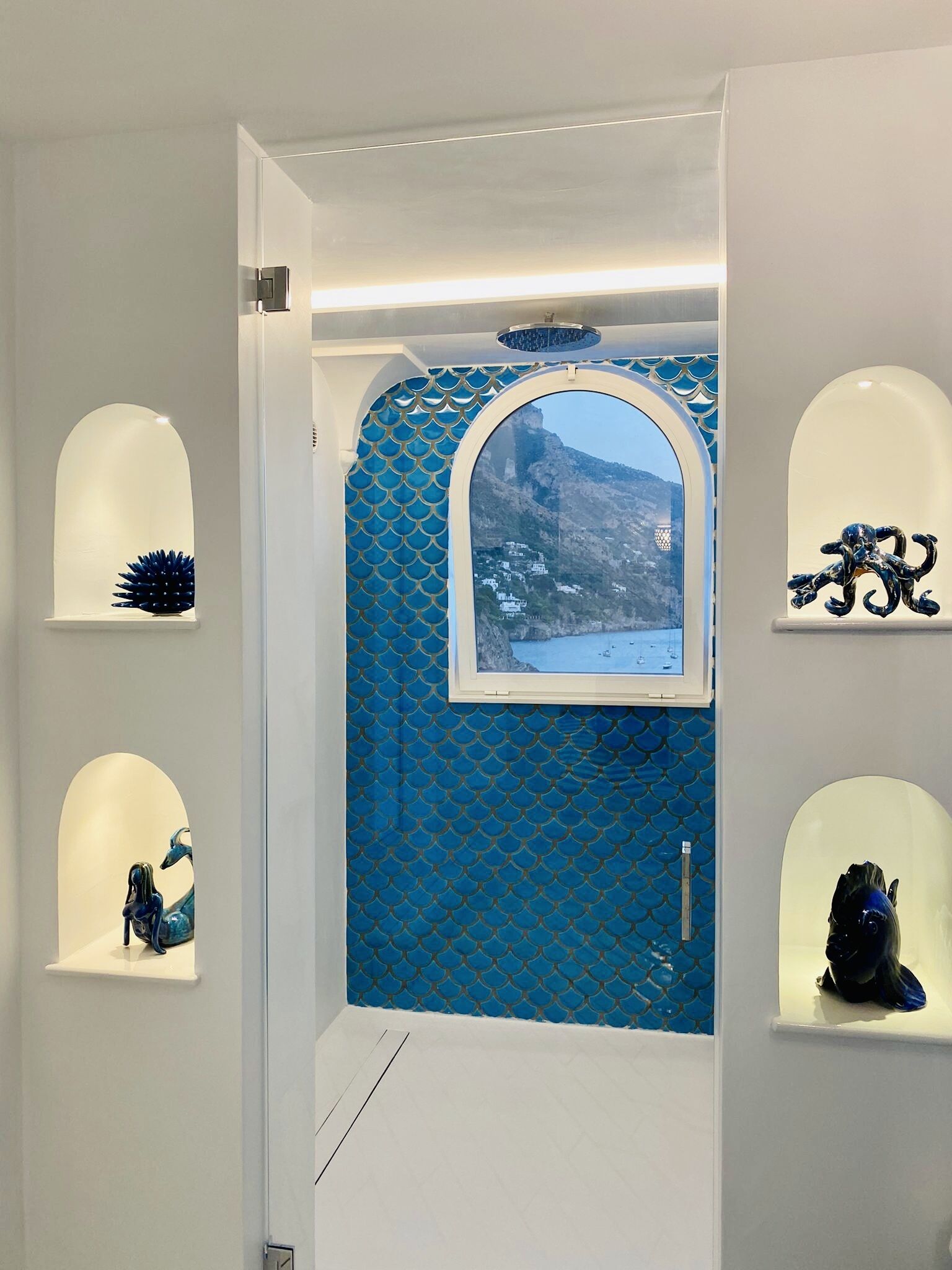 A doorway with a blue patterned door and a view of a mountainous landscape. Shelves on either side hold decorative items.