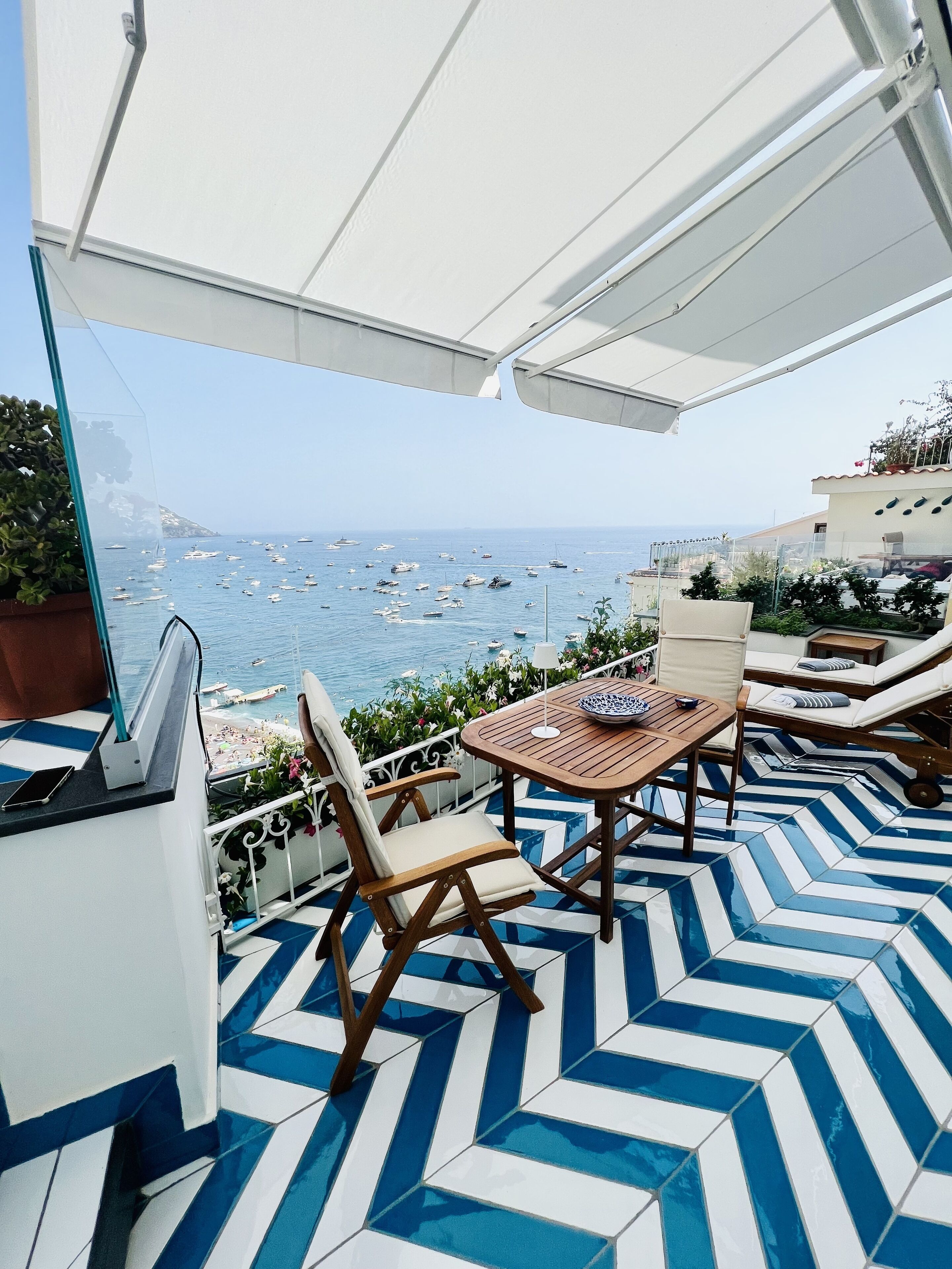 Una terraza con vistas al mar, que incluye una mesa, sillas, un suelo con diseño y una barrera de cristal transparente.