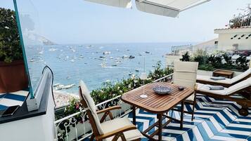 Una terraza con vistas al mar, que incluye una mesa, sillas, un suelo con diseño y una barrera de cristal transparente.