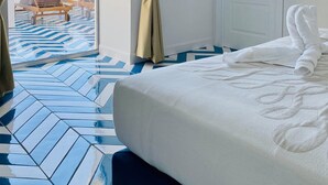Habitación de hotel con una cama, un televisor montado en la pared y vista al mar a través de una puerta abierta.