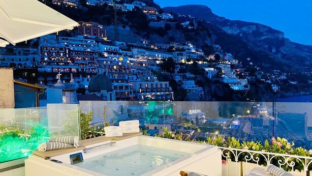 Una terraza en la azotea con un jacuzzi, una silla de descanso y vistas a un pueblo en la ladera al atardecer.