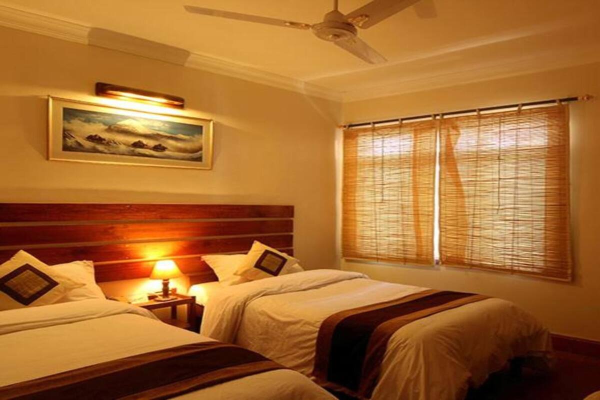 A hotel room with two beds, a ceiling fan, a painting on the wall, and a window with blinds.