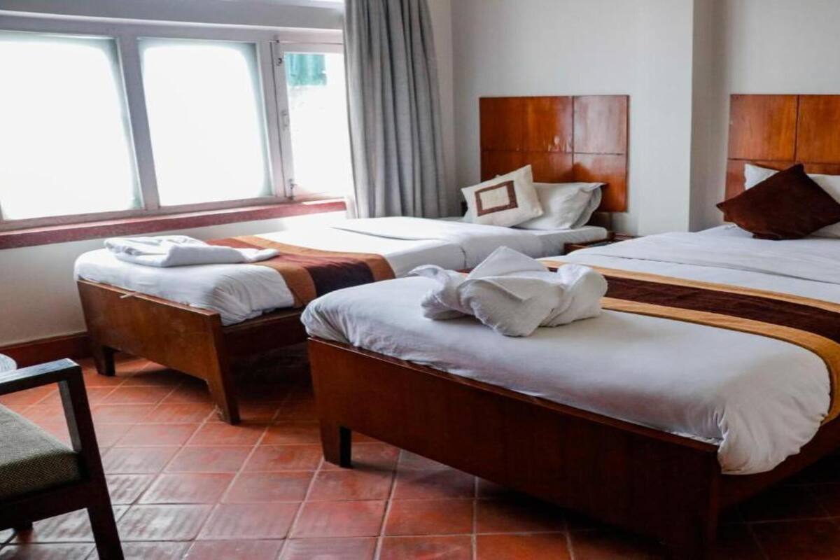 A hotel room with two beds, a wooden headboard, and a tiled floor.