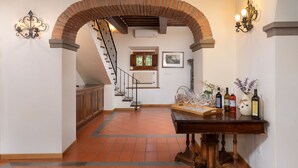 Un pasillo con un arco de ladrillo, una escalera y una mesa con botellas de vino y copas.