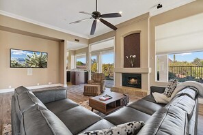 A spacious living room with a fireplace, leather sofas, a ceiling fan, and a large TV. - 6BR Estate + Guest House, Pool & Spa (Scottsdale)