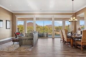 A spacious living room with a large sliding glass door leading to a patio, a dining area with a wooden table and chairs, and a sofa set. - 6BR Estate + Guest House, Pool & Spa (Scottsdale)