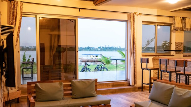 Ein Zimmer mit einer Holzbank und einer Couch, großen Schiebeglastüren und Blick auf Fahrräder sowie einen Steg am Wasser.