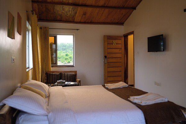 Un dormitorio con cama, ventana con cortinas, una puerta y televisor en la pared.