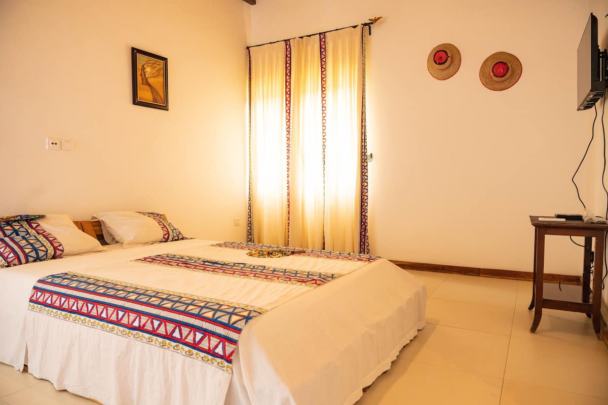 A bedroom with a bed, curtains, a wall-mounted TV, and a small table.