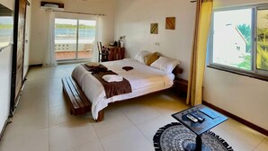 A spacious bedroom with a large bed, a round coffee table, and a view of the outdoors through a large window. - La Villa Aphro Benin (Ouidah)