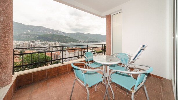 A balcony with a table and chairs, a view of a cityscape and mountains, and a tiled floor. - Sea view studio Tibor (Budva)