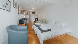 A modern hotel room with a bed, a blue armchair, a kitchenette, and a dining area. - Sea view studio Tibor (Budva)