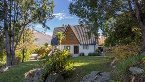 Una casa moderna con techo inclinado, rodeada de vegetación exuberante y una montaña al fondo.
