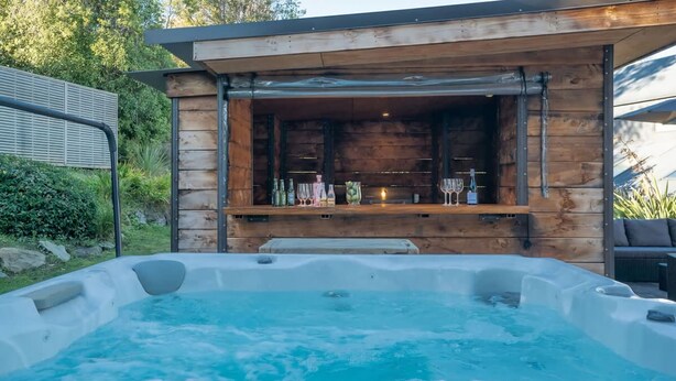 Zona de jacuzzi con terraza de madera y barra con botellas y vasos.
