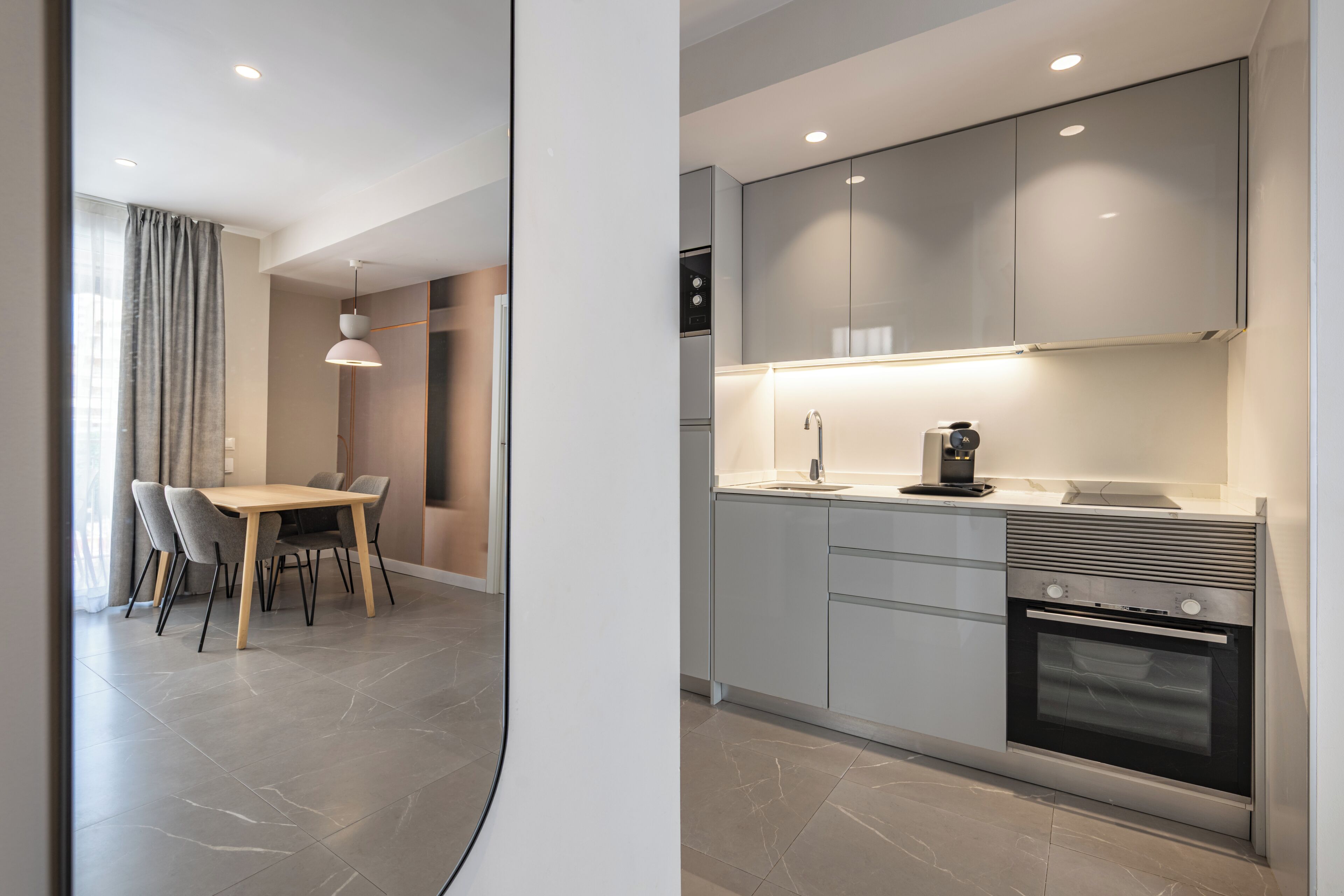 A modern kitchen with a built-in oven, a dining area with a table and chairs, and a pendant light.