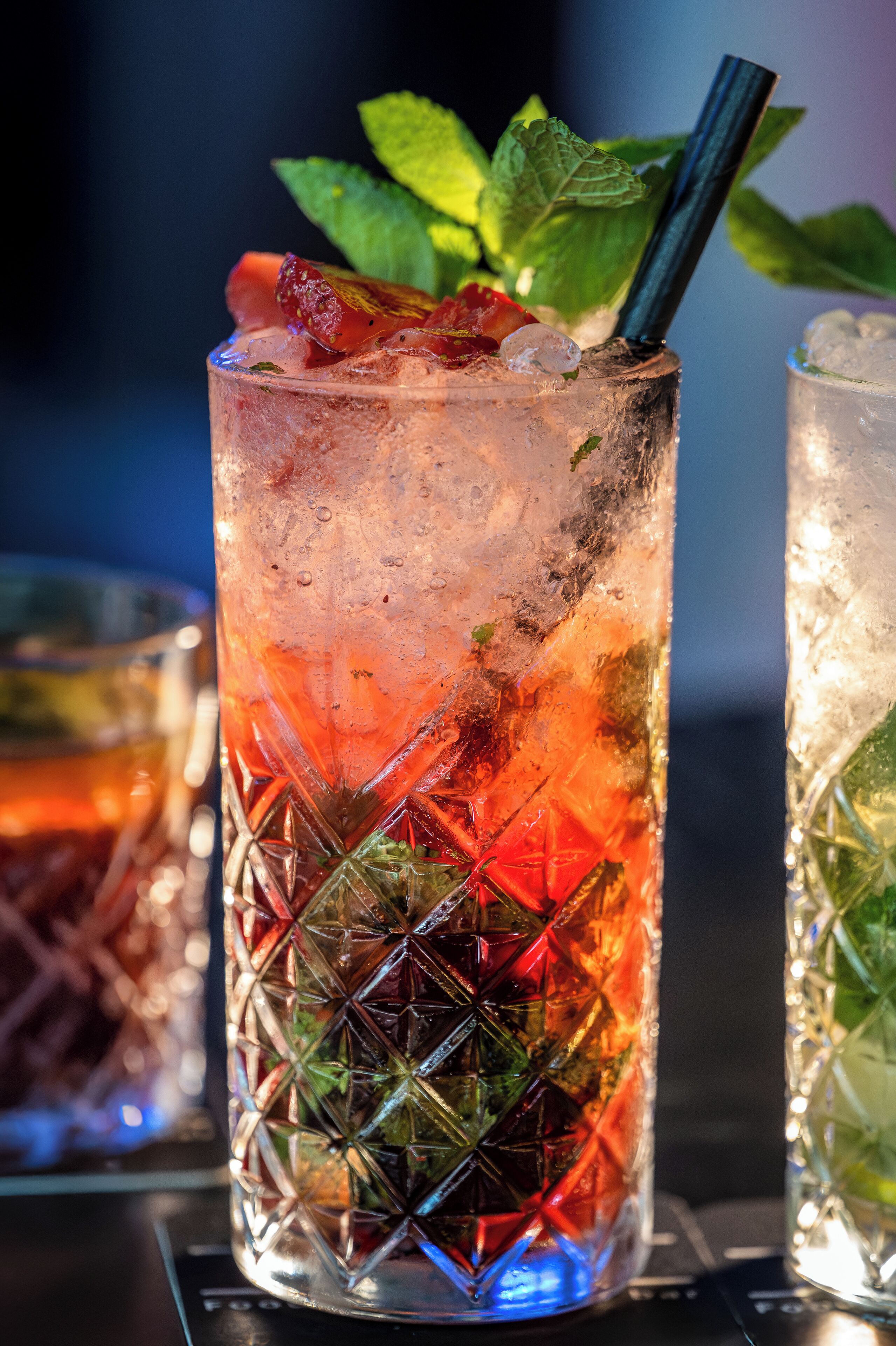Two tall glasses of iced drinks with mint leaves and a straw, placed on a table.
