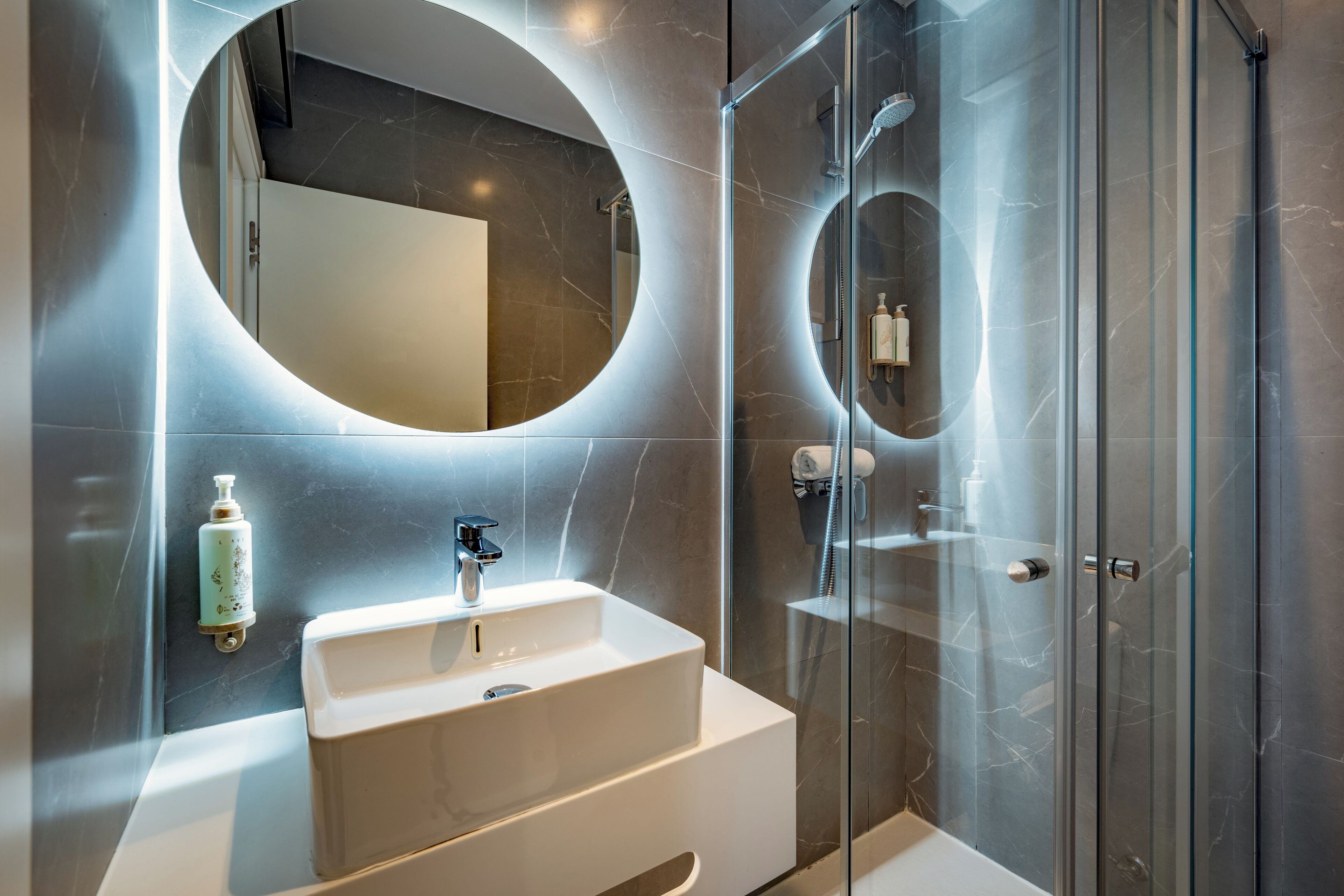 Un baño moderno con un lavabo blanco, un espejo grande y una ducha con mampara de vidrio.