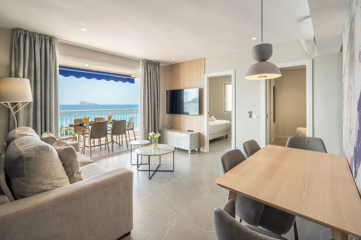A modern hotel room with a balcony, a dining area, a living room, and a bedroom.