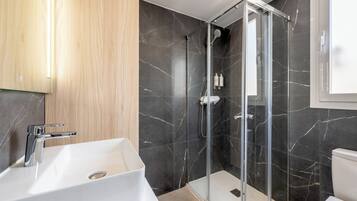 Une salle de bain moderne avec une douche à parois de verre, un lavabo blanc et des murs en marbre foncé.