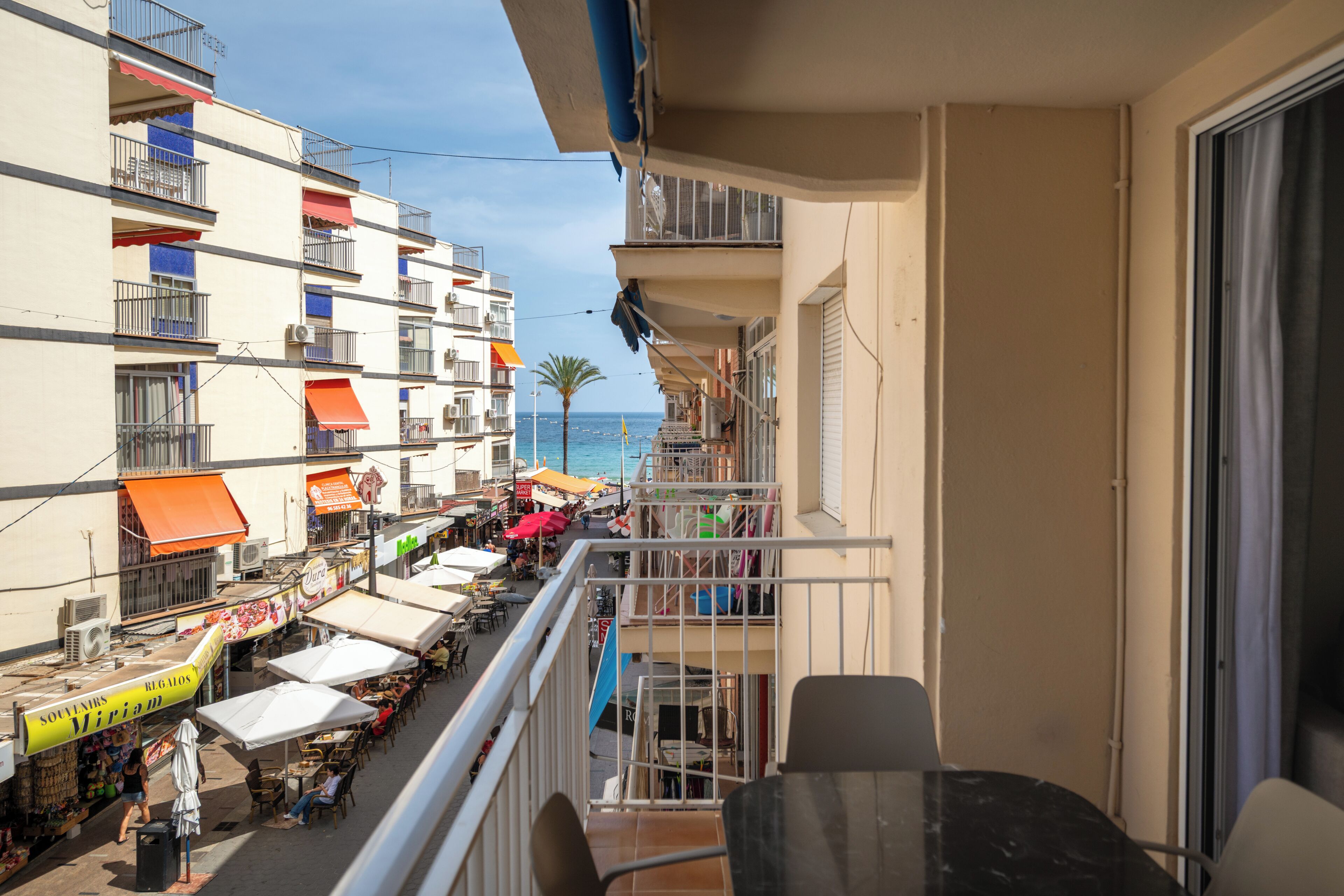 A balcony with a view of a busy street, outdoor seating, and a building with balconies.