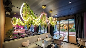En modern restaurang med en bardel, sittplatser med bekväma bänkar och bord samt hängande växter med upplysta ringar.