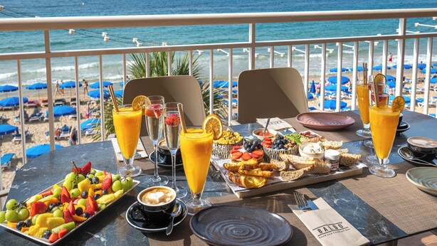 Ett bord med frukostmat, drycker och utsikt över stranden och havet.