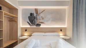 Ett modernt hotellrum med en stor säng, sängbord, en garderob i trä och ett konstverk som hänger på väggen.