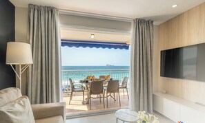 A modern hotel room with a balcony overlooking the sea, a dining area with a table set for two, and a flat-screen TV mounted on the wall. - Mara Boutique Apartments (Benidorm)