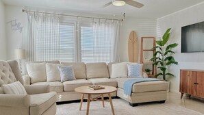 A living room with a beige sectional sofa, a round coffee table, and a ceiling fan. - The Cape (Brevard County)