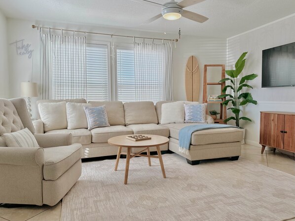 Ein Wohnzimmer mit einem beigefarbenen Ecksofa, einem runden Couchtisch und einem Deckenventilator.