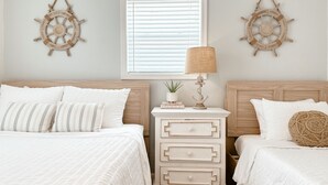 A bedroom with two beds, a nightstand with a lamp, and two wall-mounted ship wheel decorations. - The Cape (Brevard County)