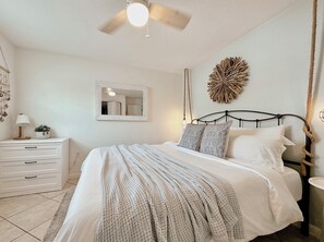 Ein Schlafzimmer mit einem Bett, einem Nachttisch mit Lampe, einem Spiegel und einer Wanddekoration.