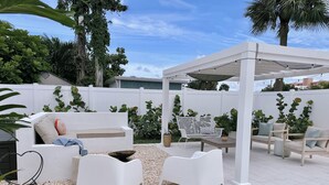 A patio area with white furniture, including a sofa and two chairs, surrounded by a white fence and various plants. - The Cape (Brevard County)