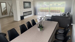 Ein modernes Wohnzimmer mit Kamin, Essbereich mit Stühlen, einer Couch und einem an der Wand montierten Fernseher.