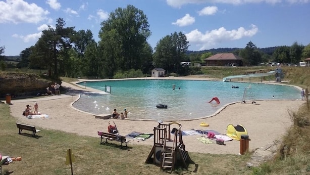 Ein Schwimmbecken mit Sandstrand, einem kleinen Gebäude und Bäumen im Hintergrund.