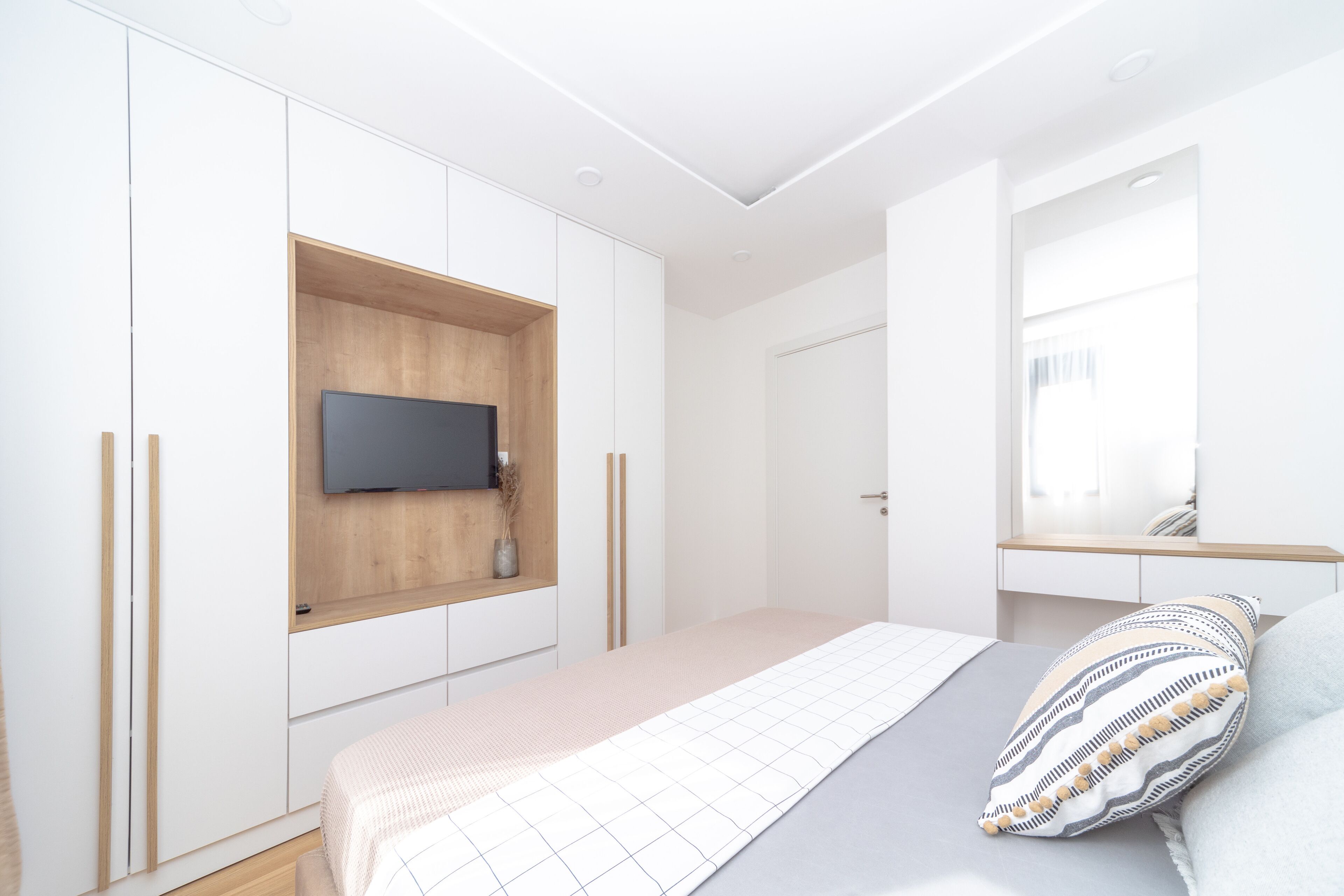 A bedroom with a bed, a TV mounted on a wooden shelf, a mirror, and a wardrobe.