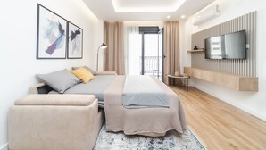 A modern hotel room with a bed, a sofa, a TV mounted on the wall, and a balcony with curtains. - Salus Hill Condo (Budva)