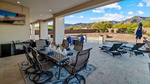 An outdoor patio with a dining table set for four, surrounded by chairs, and a pool area with lounge chairs. - An Arrow Escape! Views, Outdoor Games, Htd Pool & Spa (Gold Canyon)