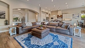A spacious living room with a large sectional sofa, a coffee table, and a blue patterned rug. - An Arrow Escape! Views, Outdoor Games, Htd Pool & Spa (Gold Canyon)