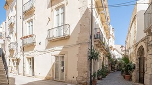 Una estrecha calle adoquinada flanqueada por edificios históricos, con balcones y macetas con plantas.