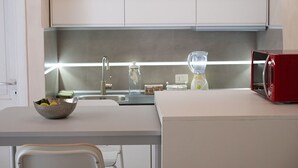 Una cocina moderna con encimera blanca, microondas rojo y un bol de fruta.