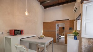 Cocina compacta con una mesa blanca, un microondas y un tazón de fruta.