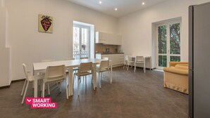 Eine moderne Küche mit weißen Schränken, ein Essbereich mit weißem Tisch und Stühlen, und ein Sofa in einem hellen Raum mit großen Fenstern.