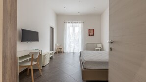 Ein Schlafzimmer mit Bett, Schreibtisch, Stuhl, Fernseher und Heizkörper.