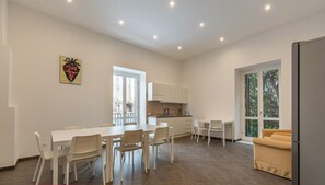 Une cuisine moderne avec des meubles blancs, un coin repas avec une table et des chaises blanches, et un canapé dans une pièce lumineuse dotée de grandes fenêtres.