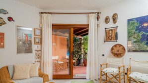 A cozy living room with a wicker sofa, a small table, and a sliding glass door leading to an outdoor patio. - Casa Flavia by Wonderful Italy (Golfo Aranci)