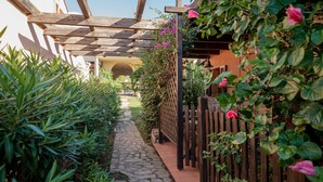 A stone pathway leading to a wooden pergola with a view of a building in the background. - Casa Flavia by Wonderful Italy (Golfo Aranci)