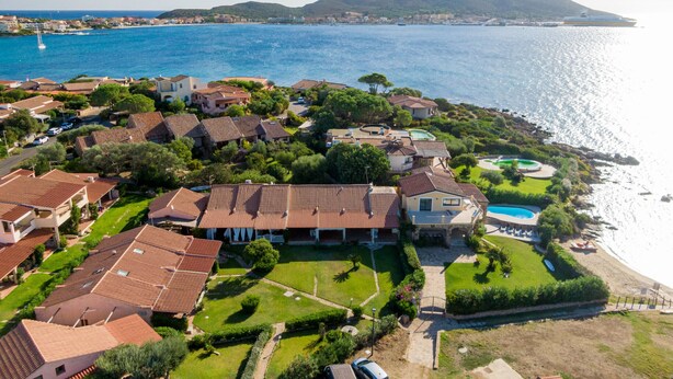An aerial view of a coastal residential area with houses, a swimming pool, and a view of the sea and mountains. - Casa Flavia by Wonderful Italy (Golfo Aranci)