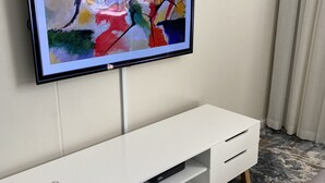 Un televisor de pantalla plana montado en una pared blanca sobre un mueble blanco con dos cajones.