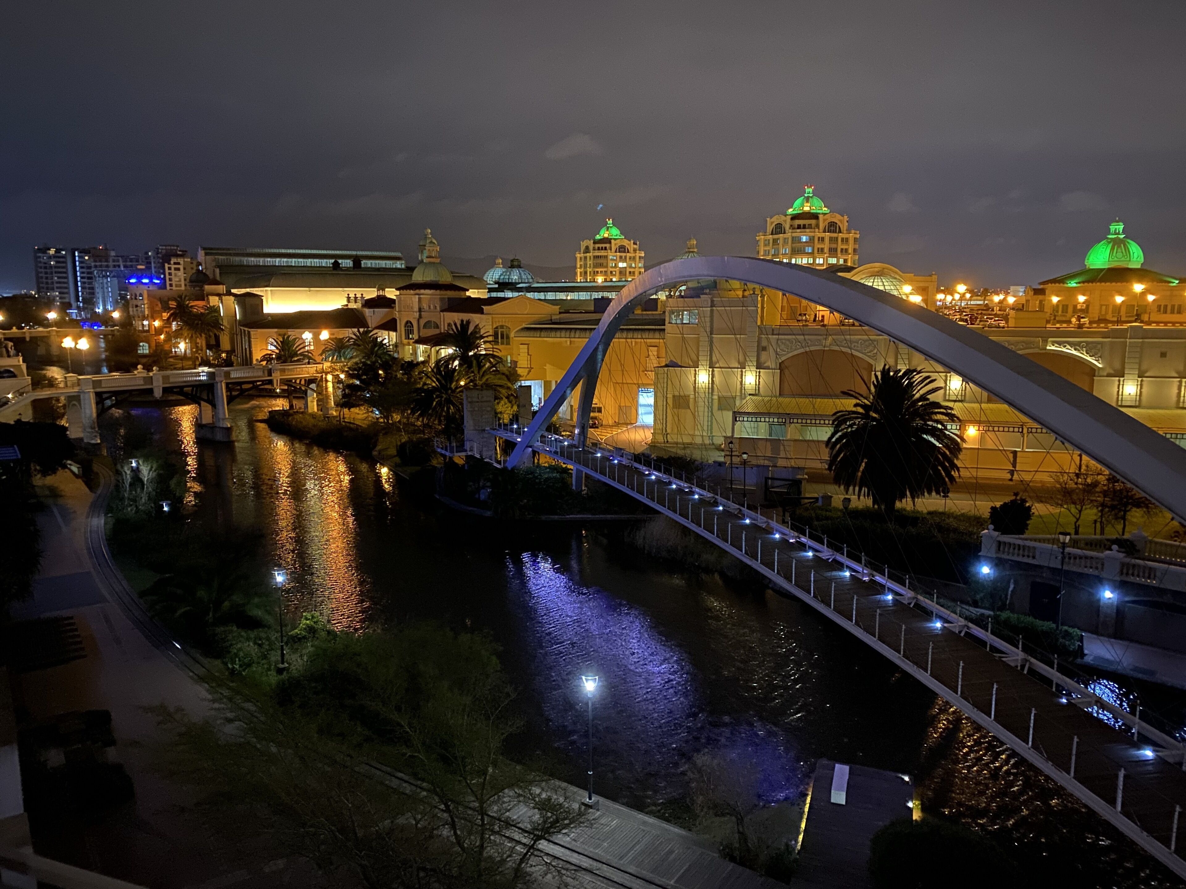 Vista nocturna de un paisaje urbano con un puente destacado, un río y edificios iluminados.